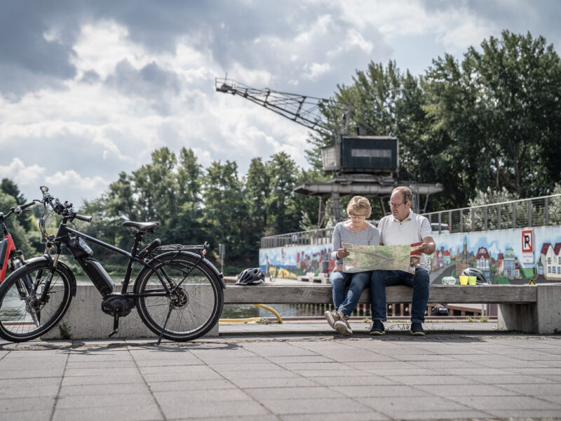 zwei Fahrradfahrer auf der Bank sitzend, gucken in eine Karte