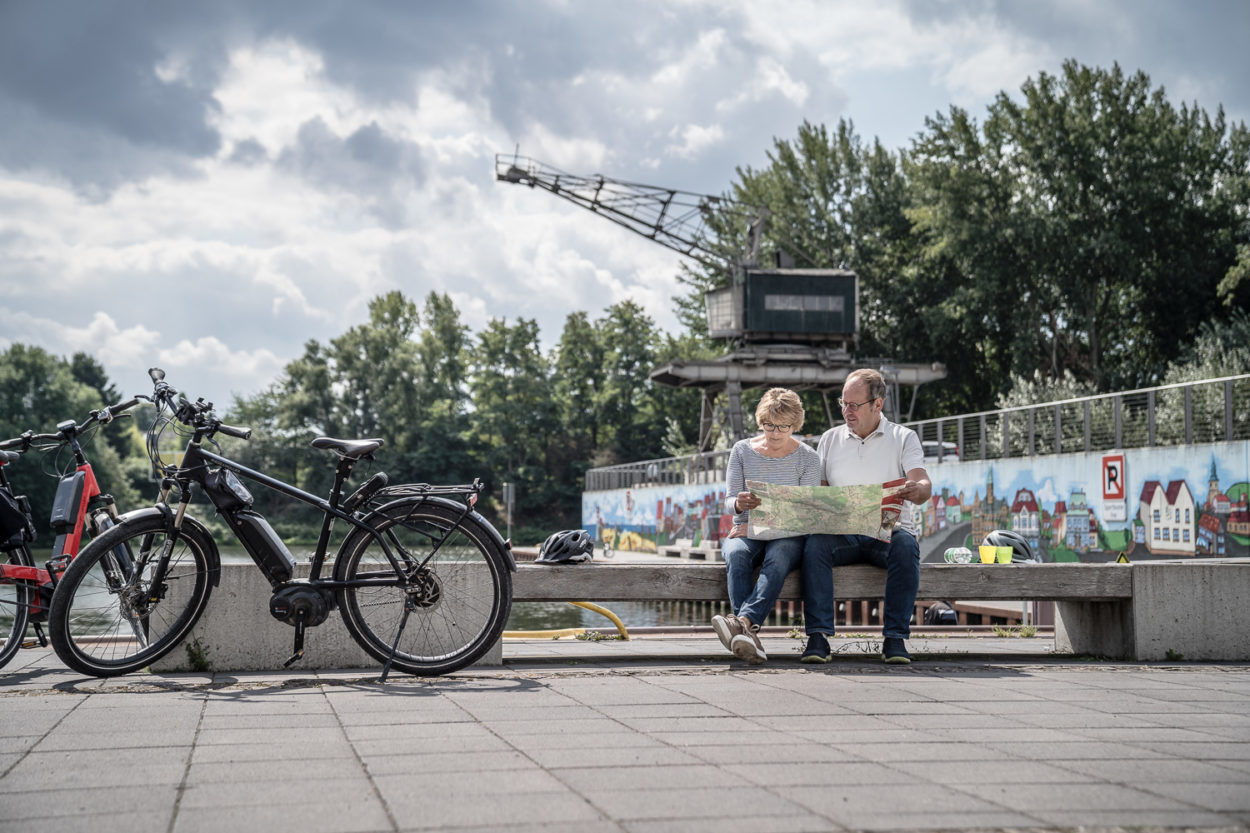 zwei Fahrradfahrer auf der Bank sitzend, gucken in eine Karte
